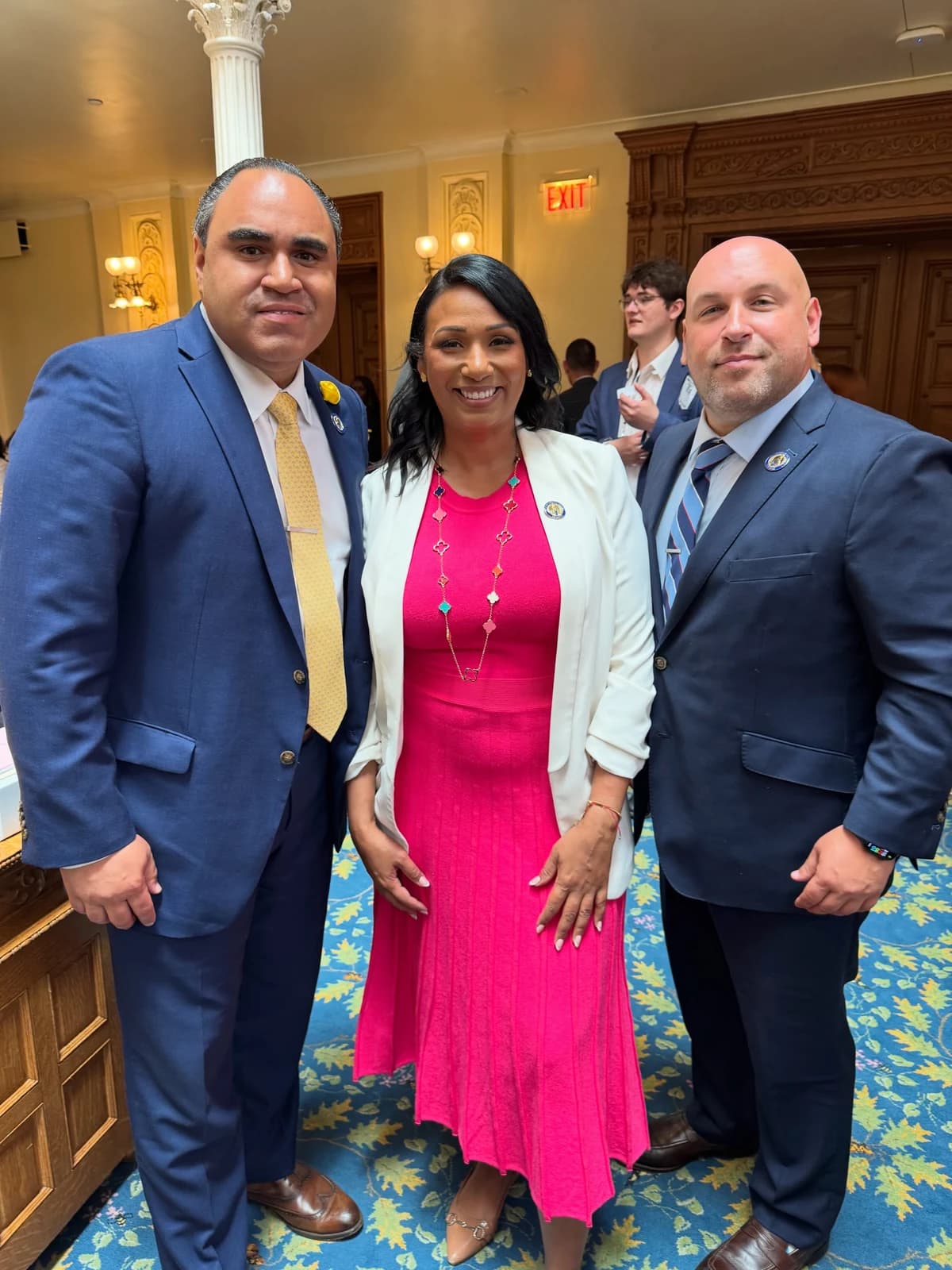 Assemblywoman Carmen Morales posing with two men in suits in the legislative chamber