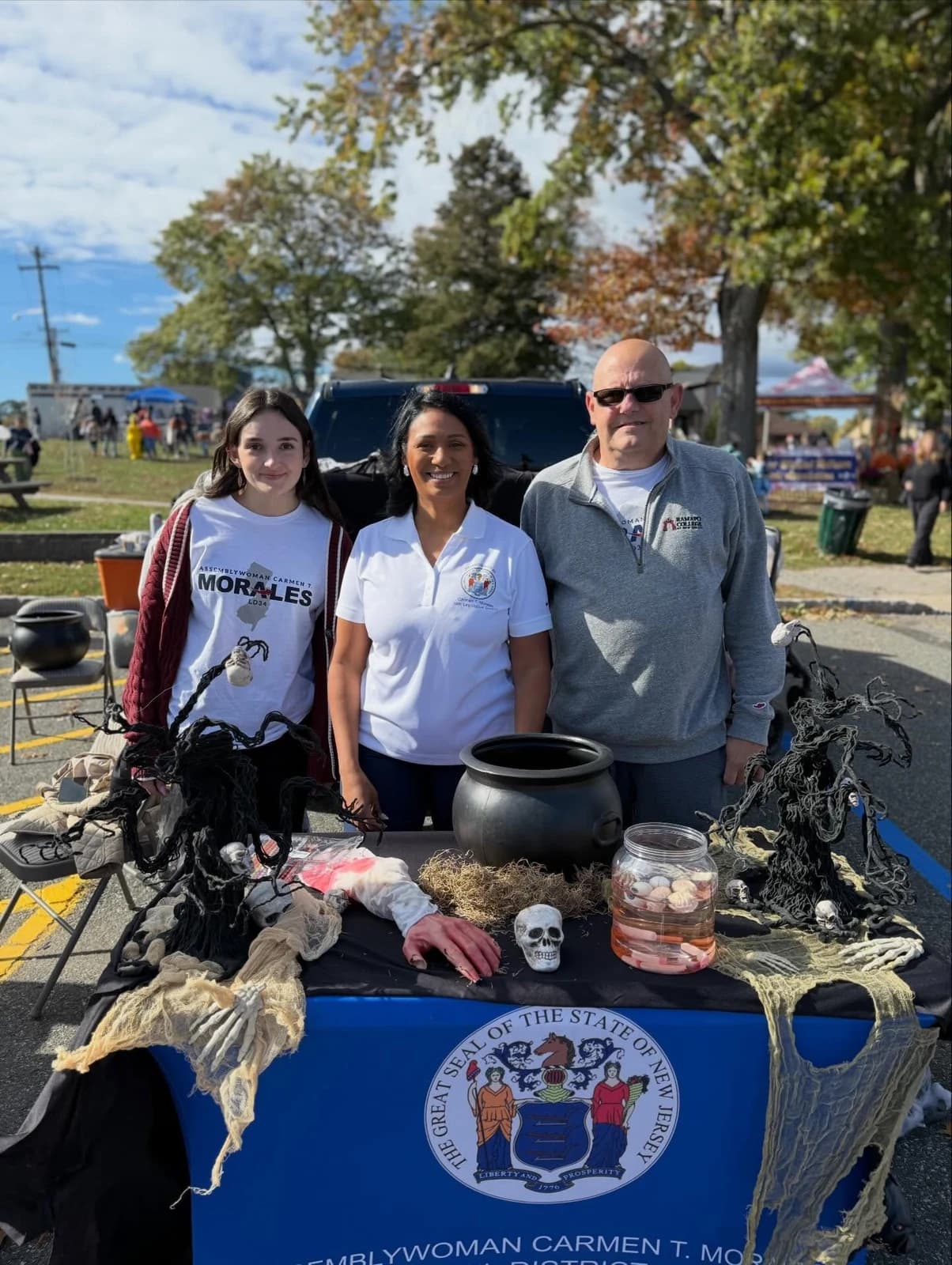 Assemblywoman Carmen Morales with two people beside an outdoor office table with seasonal decorations